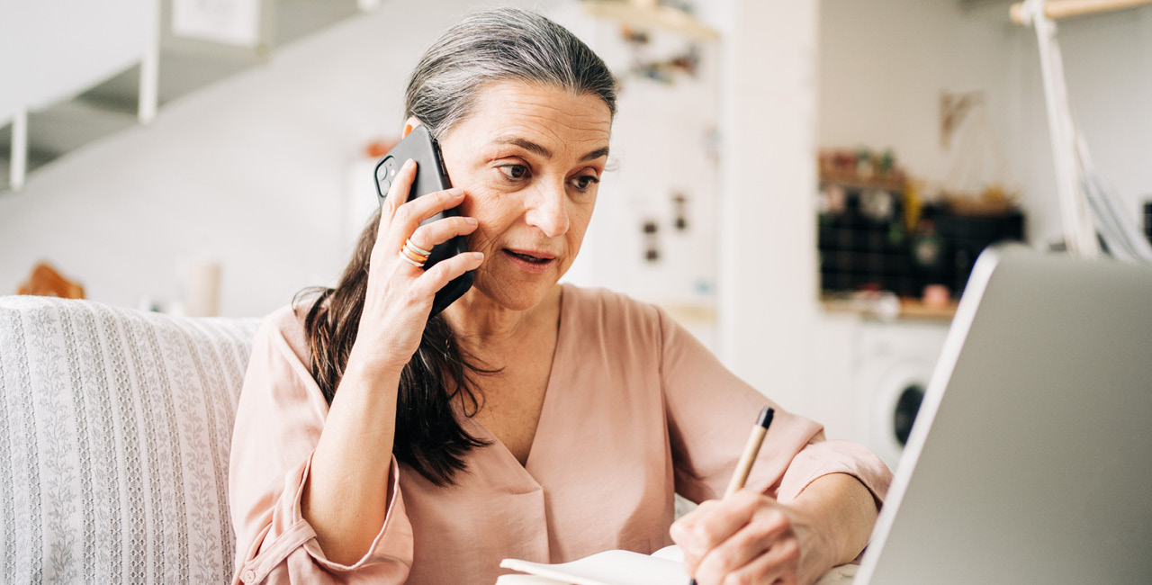 Kvinna talar i telefon framför dator